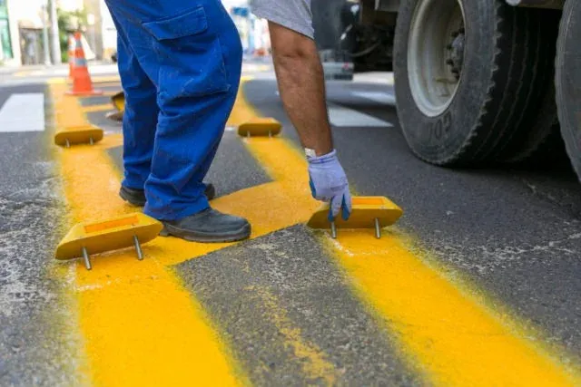 Worker applying yellow road markings on the pavement